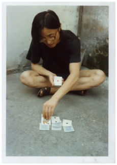 吴山专坐在街上玩牌时摄；另附英文标题「作为街头表演者，上海，中国，1984」， 1984年摄于上海